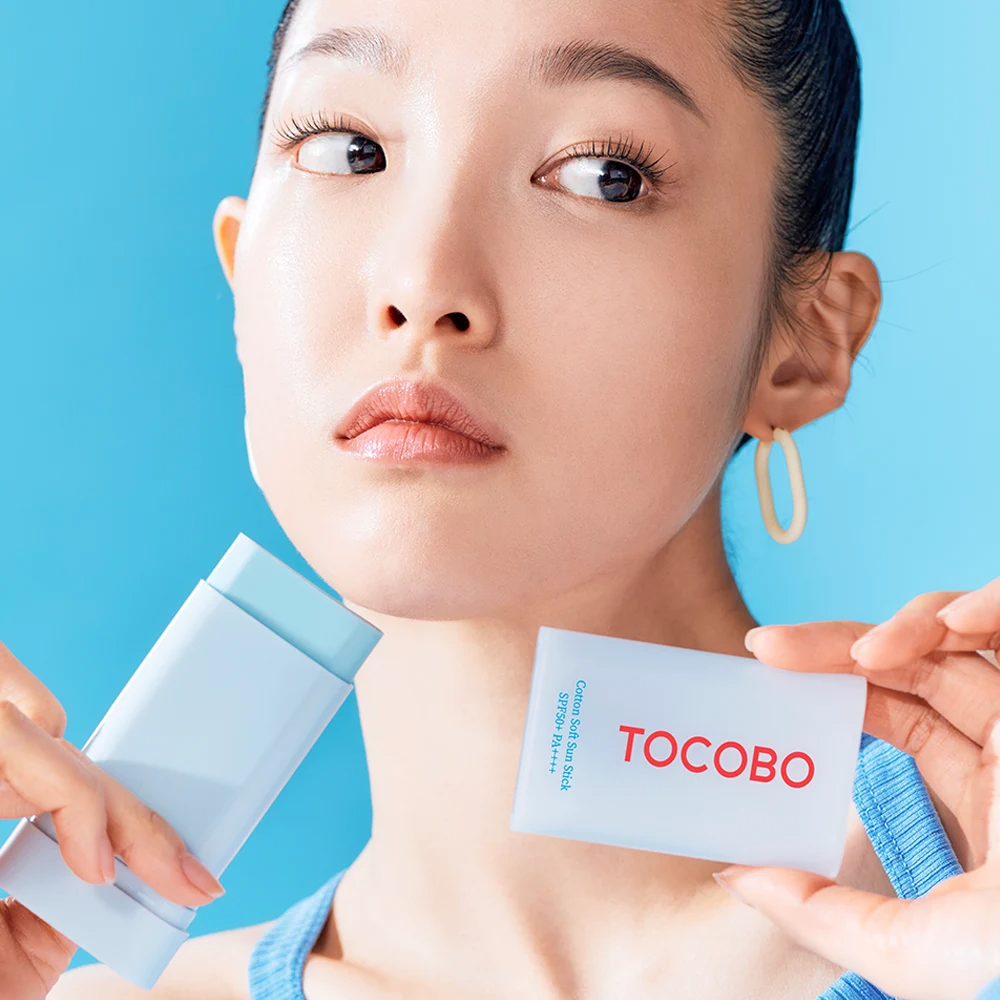 Modelo aplicando Tocobo Cotton Soft Sun Stick sobre su rostro con fondo azul.