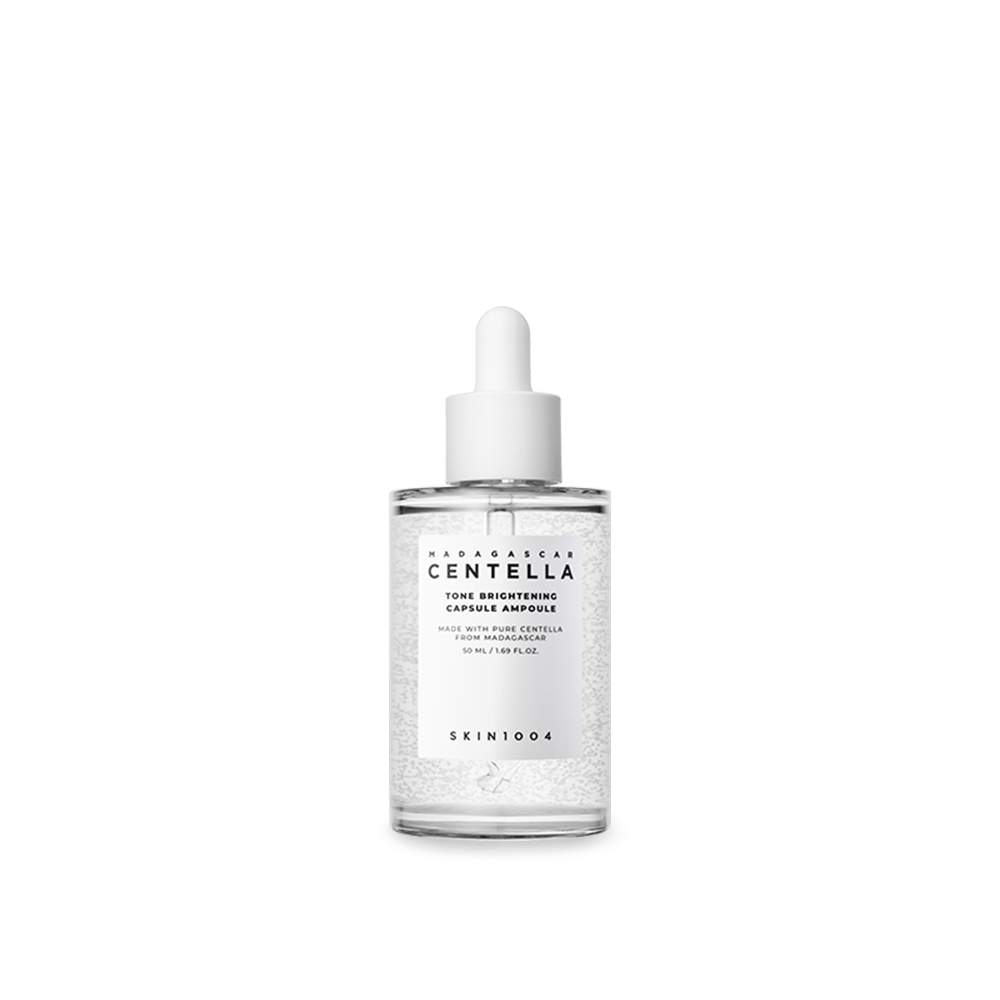 Botella transparente de 100 ml con gotero blanco y microcápsulas visibles del sérum unificador del tono con Centella de Madagascar de SKIN1004. Fotografía sobre fondo blanco que destaca la fórmula con niacinamida y ácido tranexámico para corregir manchas