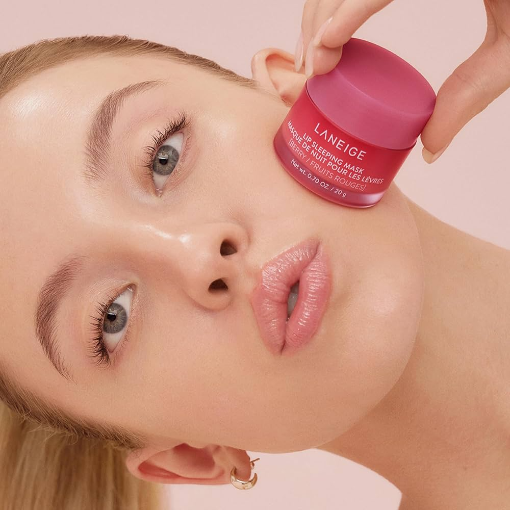 Primer plano de mujer rubia (sydney sweeney ) sujetando un tarro de Laneige Lip Sleeping Mask Berry junto a sus labios ligeramente hidratados.