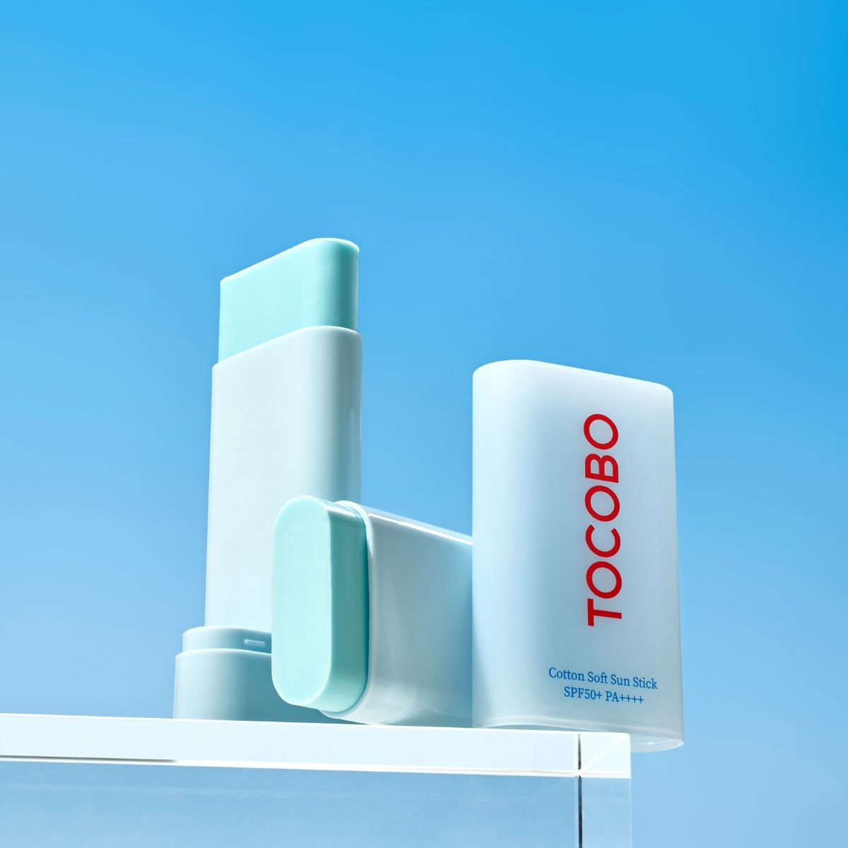 Barra Tocobo Cotton Soft Sun Stick abierta mostrando su textura, con fondo azul brillante