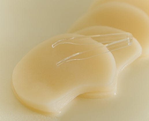 Pila de almohadillas empapadas de Skin1004 Quick Calming Pad con pinza transparente apoyada encima, fondo crema suave