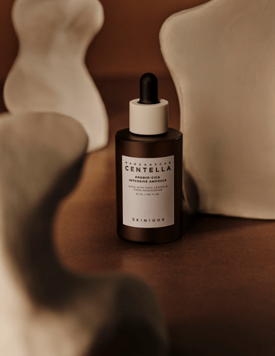 Primer plano de la ampolla Probio‑Cica de SKIN1004 apoyada sobre bloques de arcilla con fondo cálido. Se aprecia el gotero y la etiqueta del producto, que promete calma, hidratación profunda y refuerzo de la barrera cutánea gracias a la centella fermentada y las ceramidas