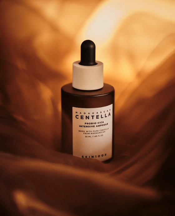 Ampolla Probio‑Cica Intensive Ampoule envuelta en una tela dorada iluminada por luz cálida. La imagen sugiere la sensación sedosa, la luminosidad y la hidratación profunda que proporciona el sérum a pieles sensibles e irritadas