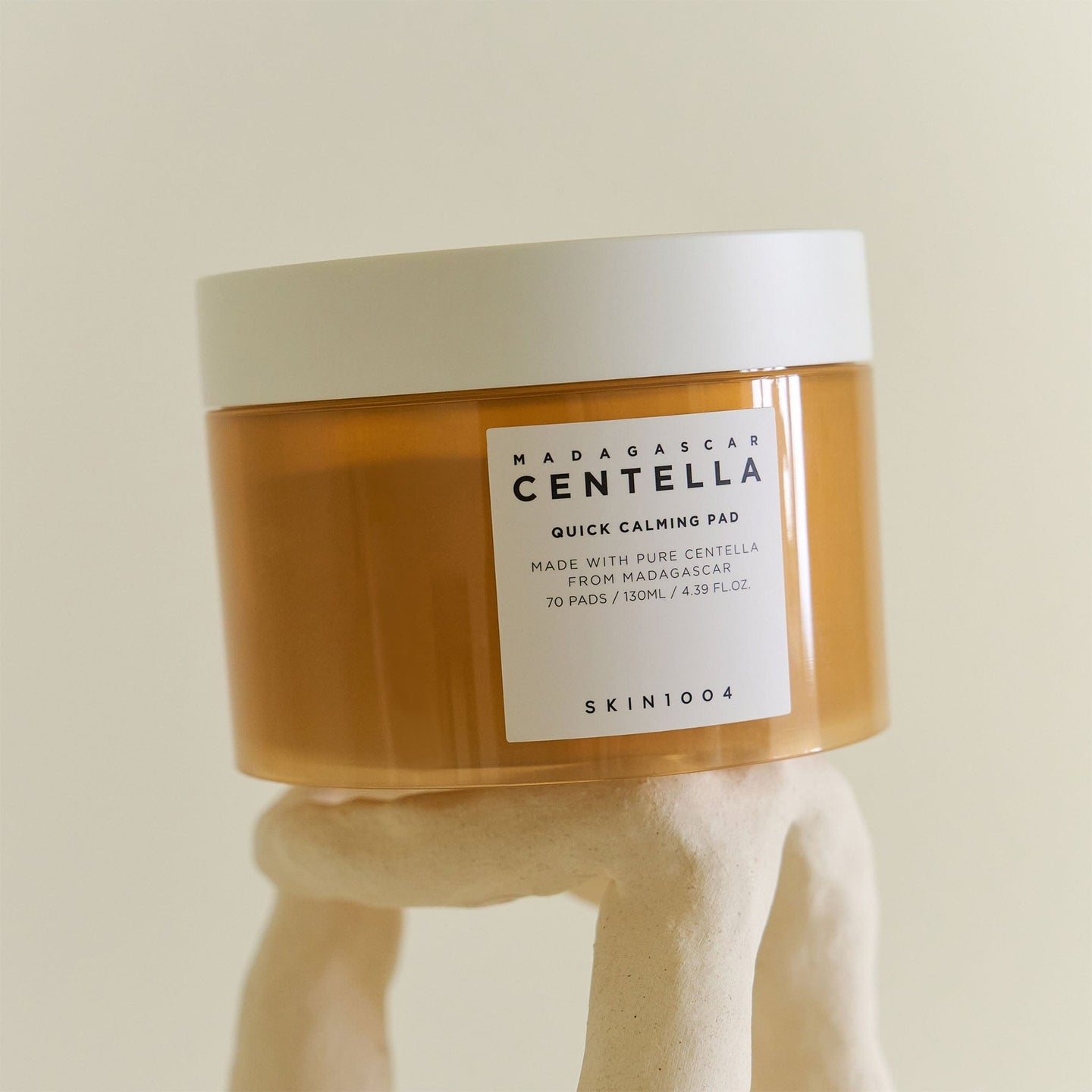 Envase cerrado de Skin1004 Madagascar Centella Quick Calming Pad (70 pads/130 ml) posado sobre un pedestal de arcilla clara, fondo beige minimalista.