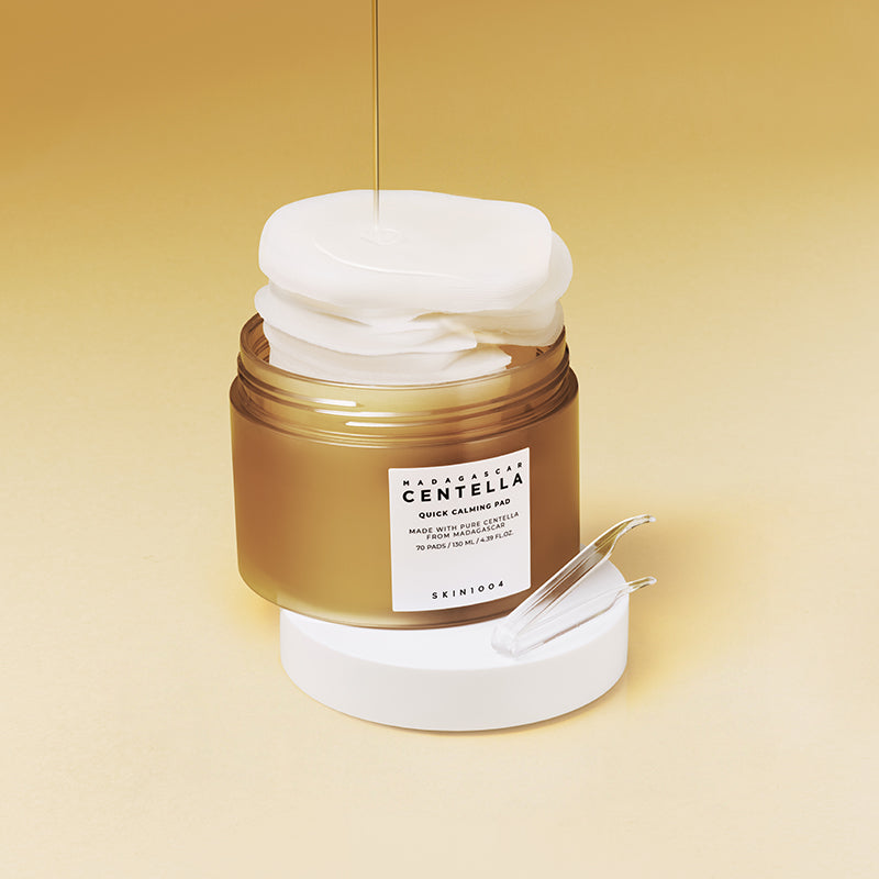 Tarro abierto de Skin1004 Madagascar Centella Quick Calming Pad de 130 ml con almohadillas blancas apiladas sobresaliendo y chorro de suero cayendo sobre ellas, sobre fondo amarillo degradado
