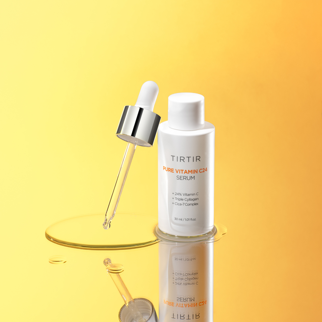Botella de Tirtir Pure Vitamin C24 Serum de 30 ml apoyada sobre un pequeño charco de suero amarillo, con pipeta plateada goteando una gota en primer plano, sobre fondo degradado amarillo