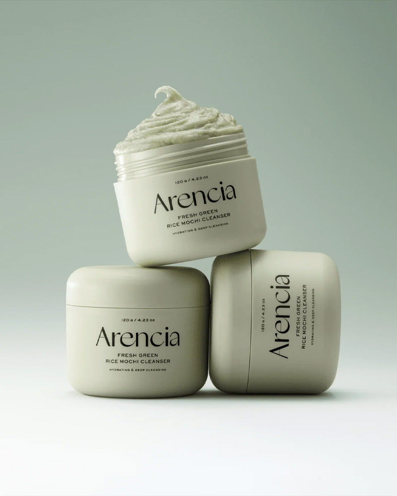 Tres envases del Arencia Fresh Green Rice Mochi Cleanser apilados en forma estética, uno de ellos abierto mostrando la textura verde densa, sobre fondo verde claro minimalista.