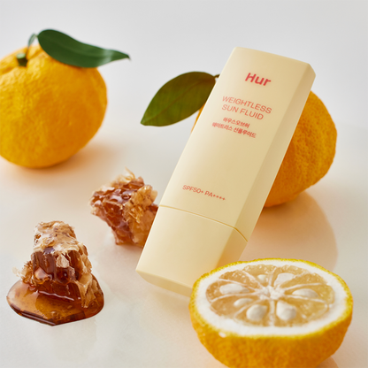 Tubo amarillo del protector solar House of Hur junto a rodajas de cítricos y miel, sobre fondo claro, evocando frescura y luminosidad.