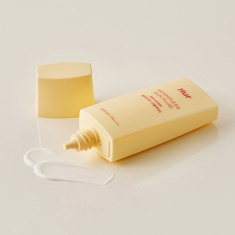 Tubo del protector solar House of Hur destapado sobre superficie beige, con crema blanca extendida al lado, mostrando fluidez y suavidad.