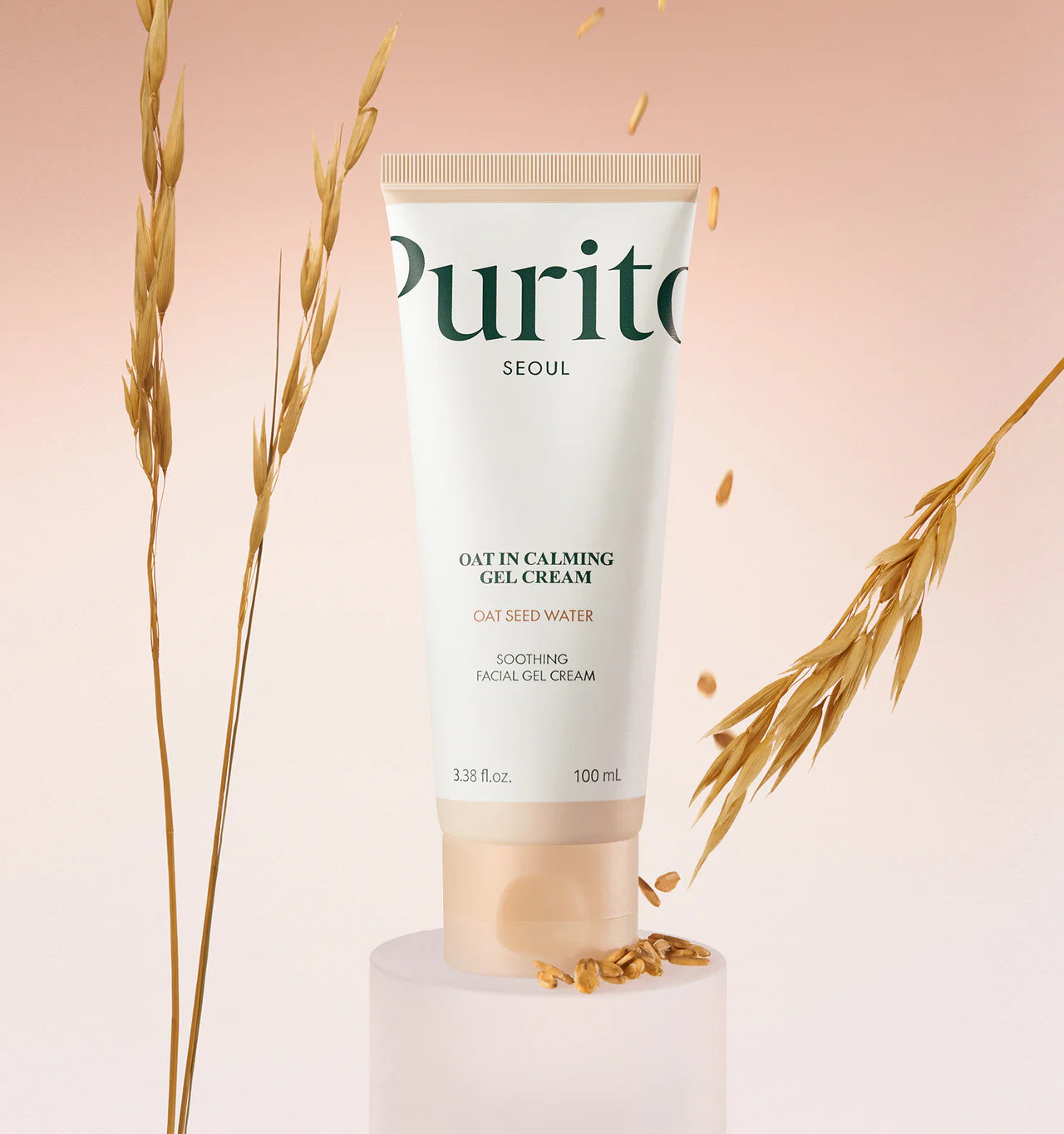 Tubo de Purito Oat-In Calming Gel Cream sobre pedestal blanco, rodeado de espigas y granos de avena sobre fondo rosa degradado.