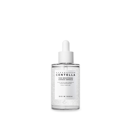 Botella transparente de 100 ml con gotero blanco y microcápsulas visibles del sérum unificador del tono con Centella de Madagascar de SKIN1004. Fotografía sobre fondo blanco que destaca la fórmula con niacinamida y ácido tranexámico para corregir manchas