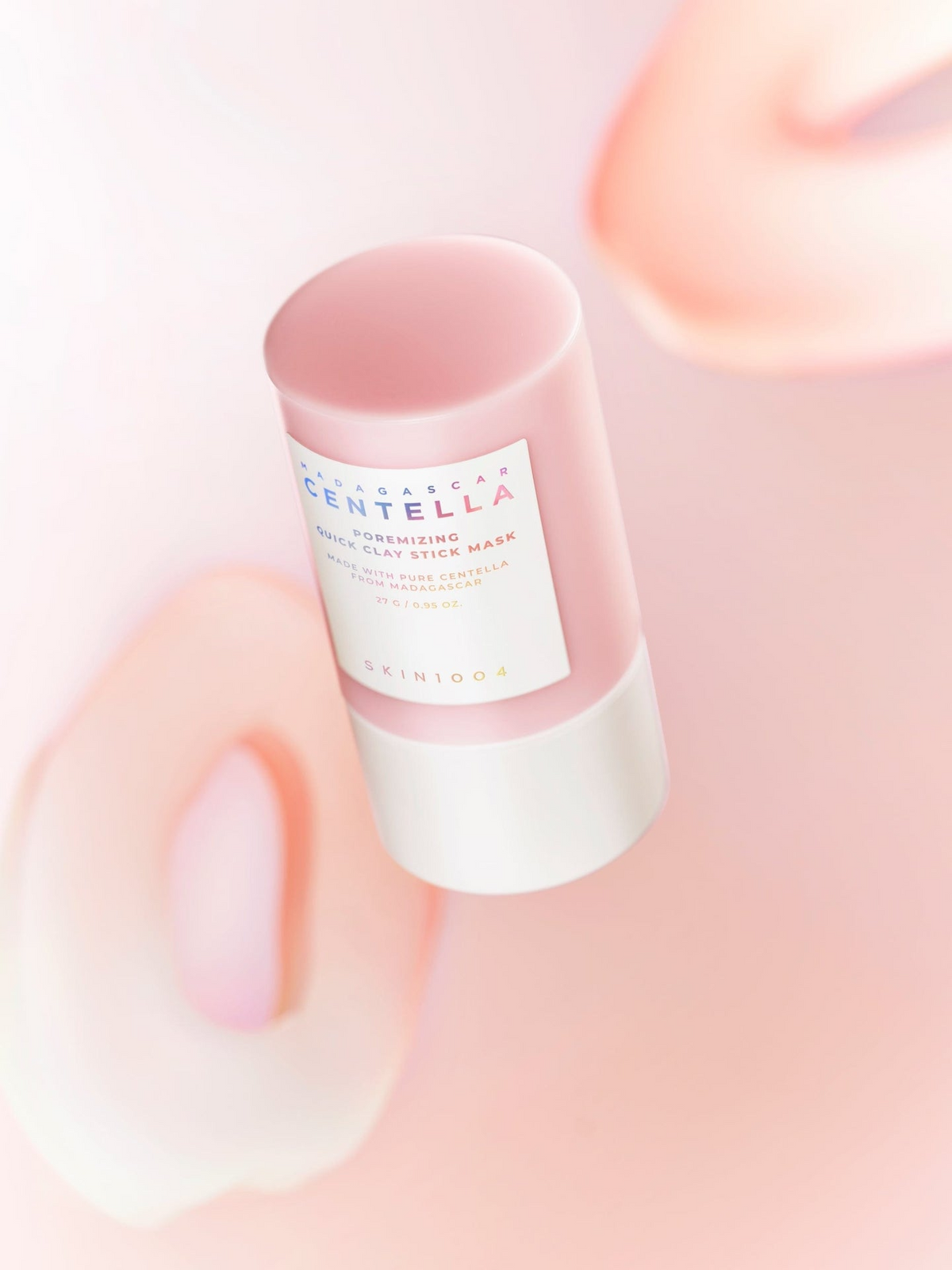 Envase del producto Skin1004 Madagascar Centella Poremizing Quick Clay Stick Mask flotando sobre fondo rosado difuminado, estilo editorial minimalista.