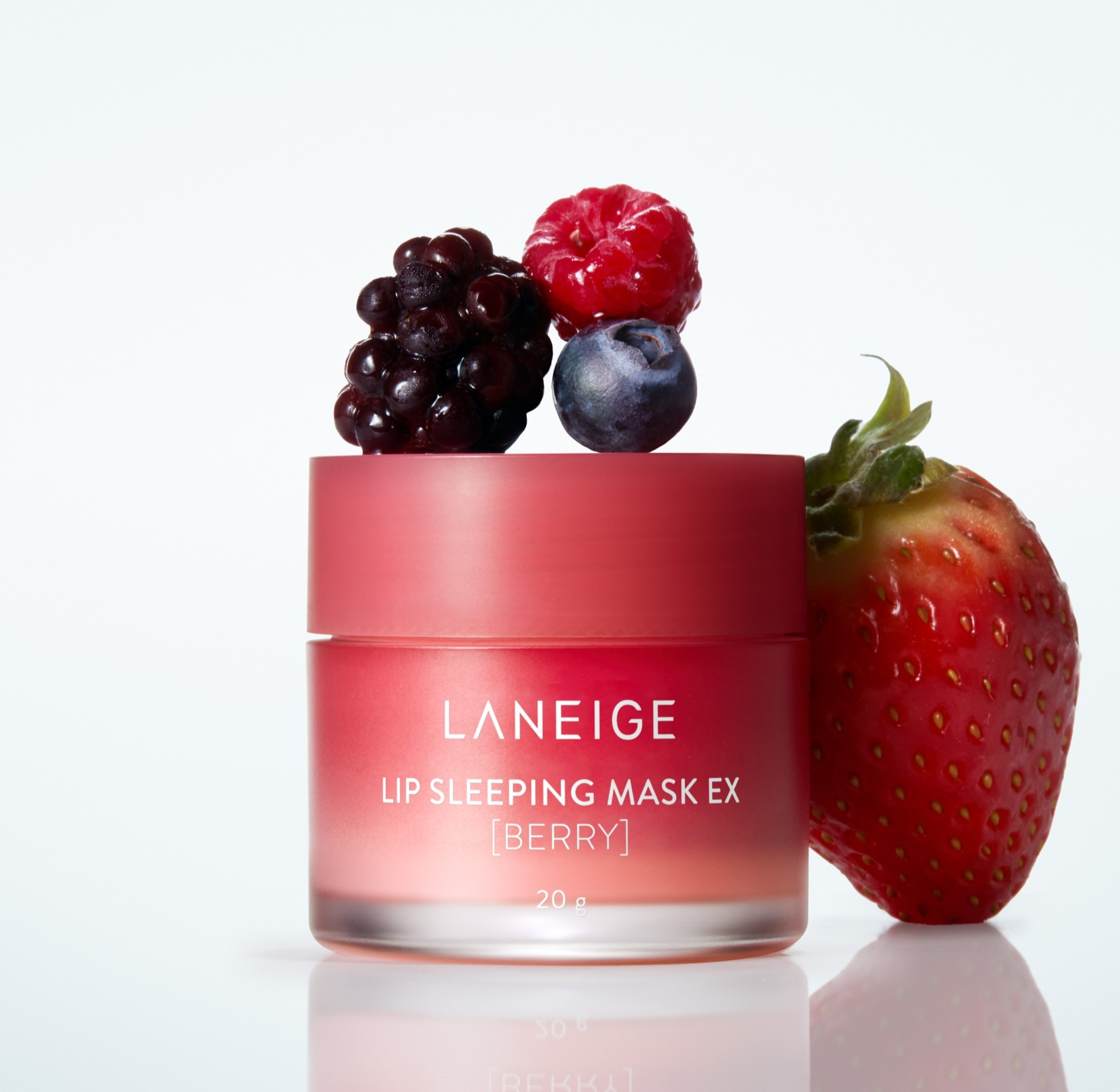 Tarro de Laneige Lip Sleeping Mask EX [Berry] de 20 g con tapa rosada mate, coronado por una mezcla de frambuesa, mora y arándano, apoyado junto a una fresa en el fondo blanco.