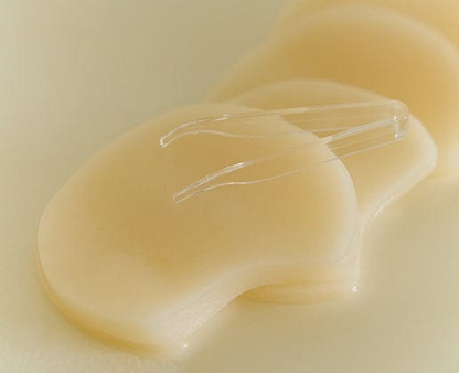 Pila de almohadillas empapadas de Skin1004 Quick Calming Pad con pinza transparente apoyada encima, fondo crema suave