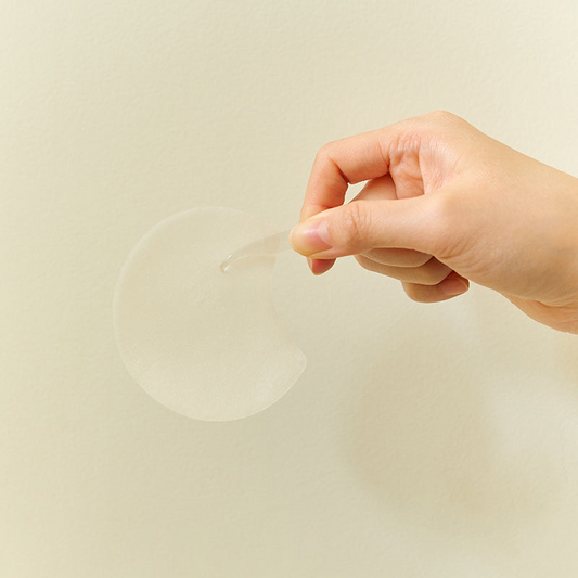 Mano usando una pinza transparente para extraer una almohadilla redonda de Skin1004 Centella Quick Calming Pad contra un fondo beige neutro.