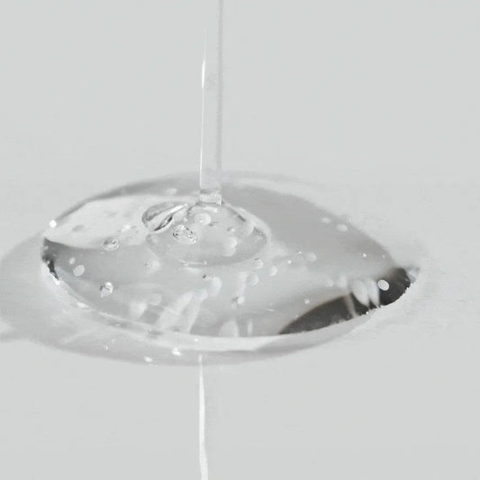 Primer plano de una gota transparente del sérum Tone Brightening Capsule Ampoule vertida en una superficie. Se observan microcápsulas suspendidas que contienen Madewhite™ encapsulado, niacinamida y ácido tranexámico para tratar manchas y unificar el tono